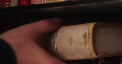A person's hand pulls out an old hardcover book from the library