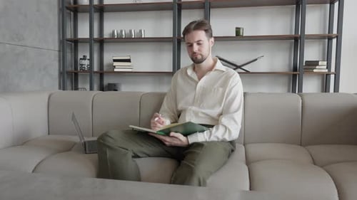 Man Writing In Notebook On Couch Focused On Creative Thought In Stylish Home