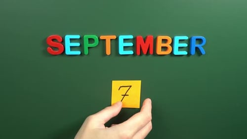 Hand sticking a sticker 7 September calendar day on school board. 7 date of September. Seventh day
