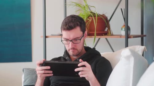 Young Adult Male Plays Handheld Video Game on Couch
