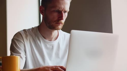 View of a Young Frowning Programmer Who is Busy Writing Code for a Mobile Application A Male