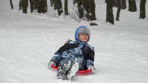 Slow motion of a cheerful boy riding down a snowy hill on his plastic sled