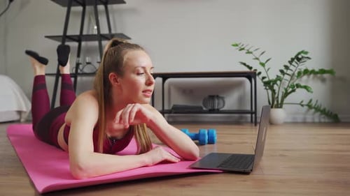 Zu Hause trainieren Junge Frau mit Laptop schaut sich Video an, Fitnessunterricht macht Plankenübungen