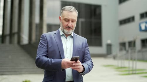 Successful senior investor with mobile phone outside office building Middle-aged businessman
