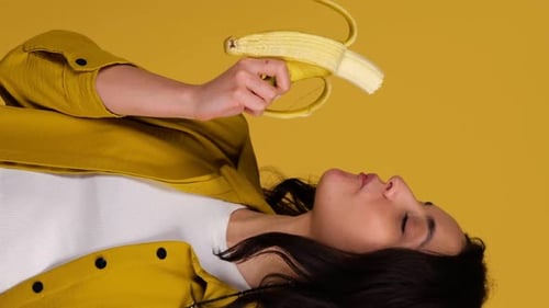 Smiling Beautiful Woman Enjoying While Eating Banana Posing in Studio Isolated on Yellow Background