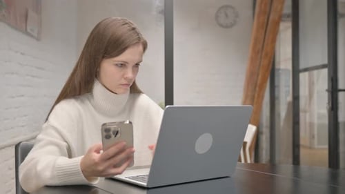 Woman Using Laptop and Phone in Home Office