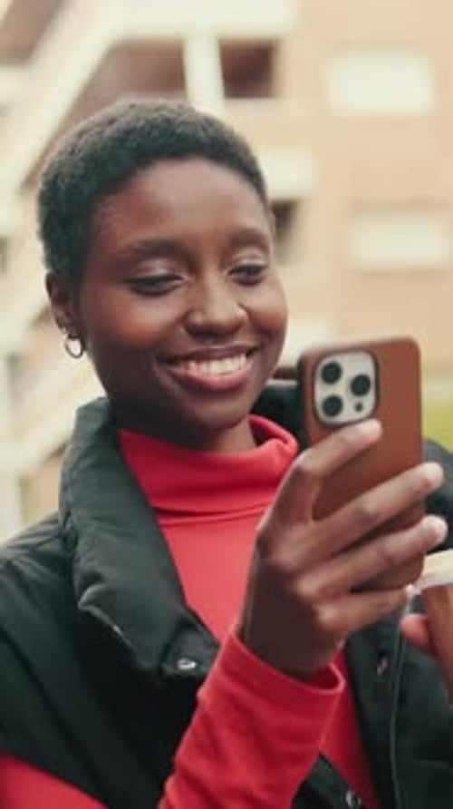 Vertical video, woman with cup of coffee in her hands texting on mobile phone