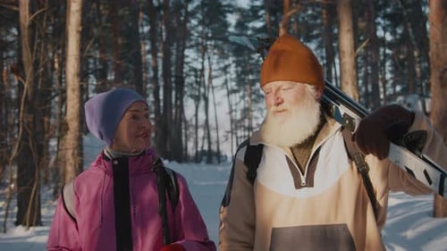 Senior Man and Woman with Skis Walking and Talking in Snowy Forest