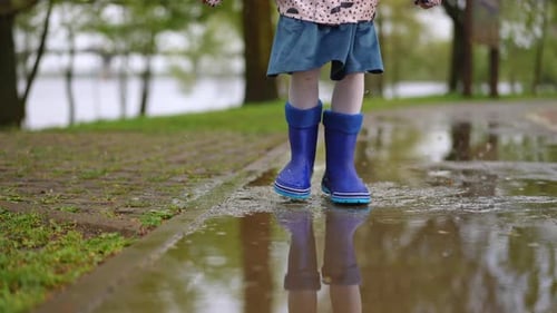 A Joyful Child Wearing Colorful Rain Boots is Happily Splashing in a Large Puddle on a Rainy Day