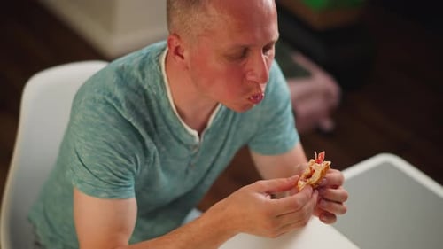 Aerial View of Adult Man Eating Snack Indoors at White Table with Blurry Background
