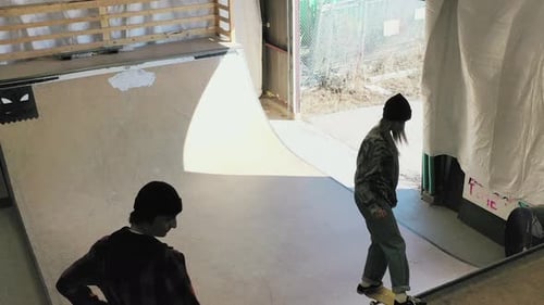 Teenage girl skateboarding on ramp at indoor skate park with friend watching