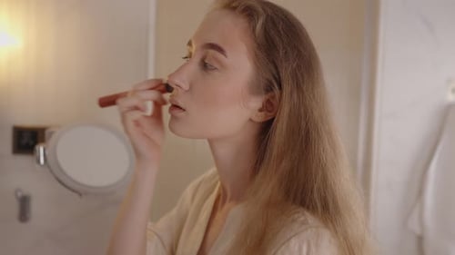Woman Applying Makeup with Brush in Bathroom Mirror