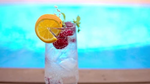 Mojito cocktail glass with ice and cherry and mint, soda and gin near a blue pool close up