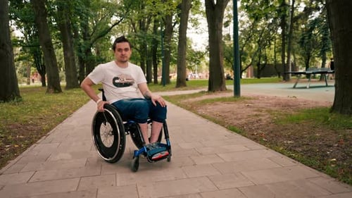 A young man in a wheelchair walks through a city park, stopped on an alley and looks intently