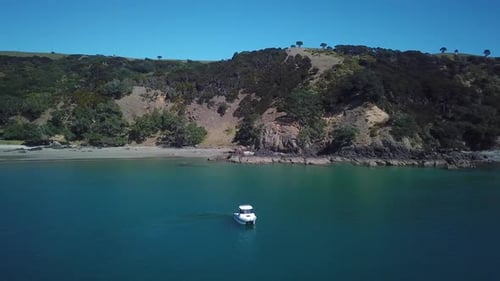Aerial, flying away from a fishing boat with beach and mountain as background on a beautiful sunny d