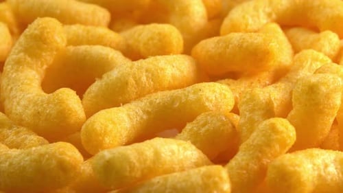 Cheesy corn sticks rotates on plate close up low light. Crispy cheese snack. Crispy fluffy corn