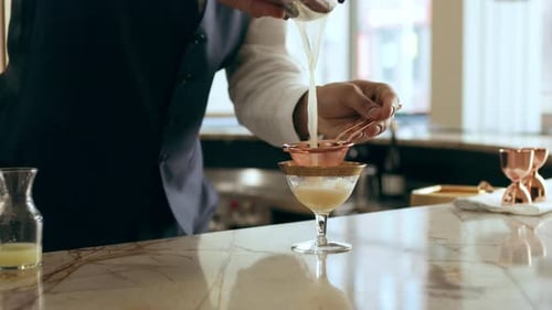 Bartender pouring cocktail through strainer on bar