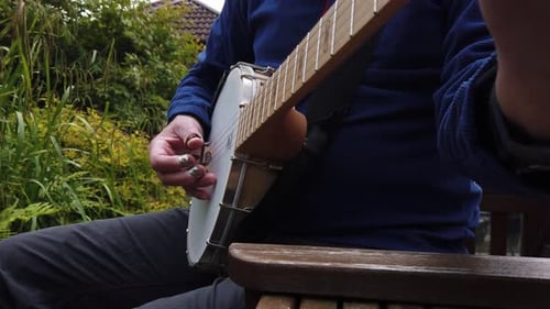 Man relaxing on garden seat finger picking a tune on the banjo