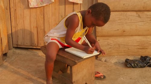 Africa school education learning concept: young kid studying alone doing homework in remote poor afr