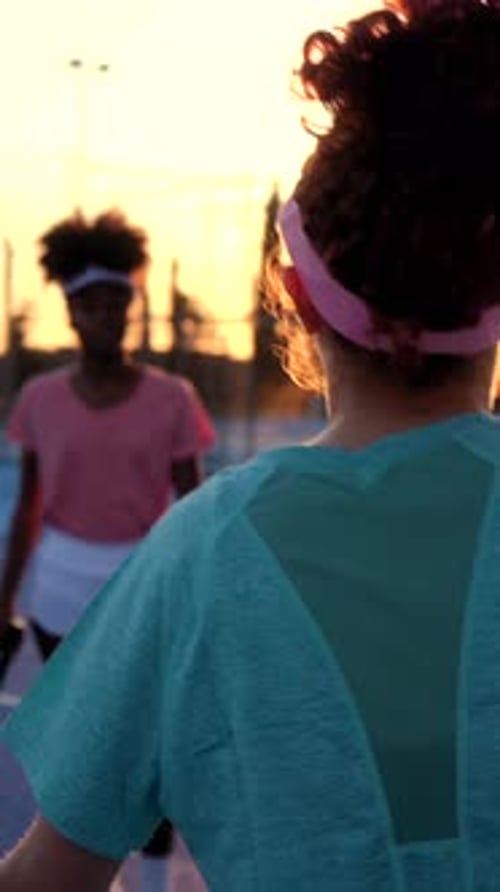 Golden hour illuminates two female tennis players as they converse on the court, likely discussing s