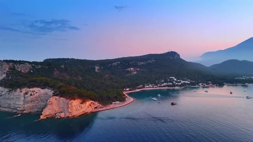 Approaching an idyllic rocky green shore of the Mediterranean Sea. Yachts are on the waterscape.