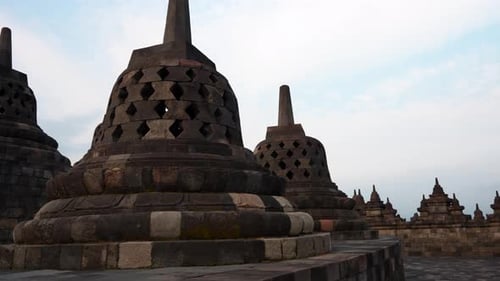 Pan shot of iconic bell-shaped stupas on top of Borobudur temple at sunset