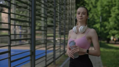 Young Woman Stands with Water Bottle in Park