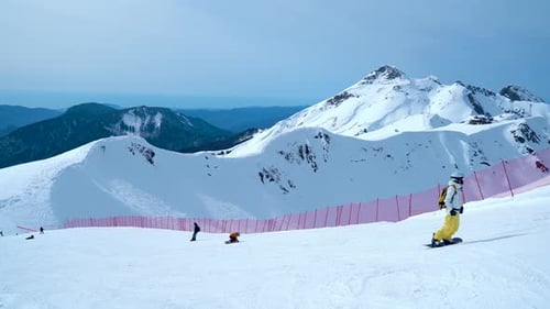 A Man In A Yellow Jacket Rides A Snowboard From The Mountain