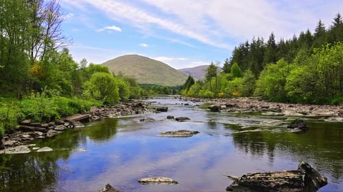 Over a river stream with dense green foliage on the river banks and Scottish highland hills