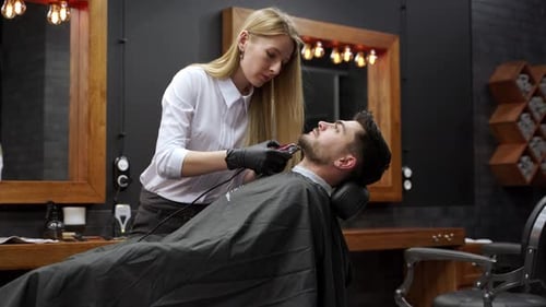 Woman Barber Grooming Man's Beard in Barbershop