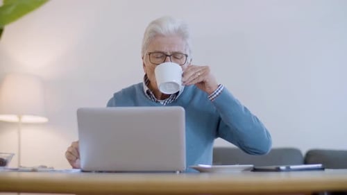 Senior Man Using Laptop and Drinking Coffee Indoors