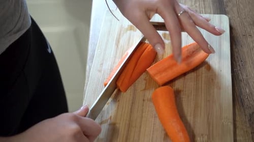 Woman Slicing Carrots with Knife on Cutting Board