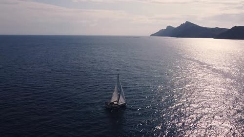 Sailboat sailing by coastline seashore against sunset and mountains. Sail boat in the south coast