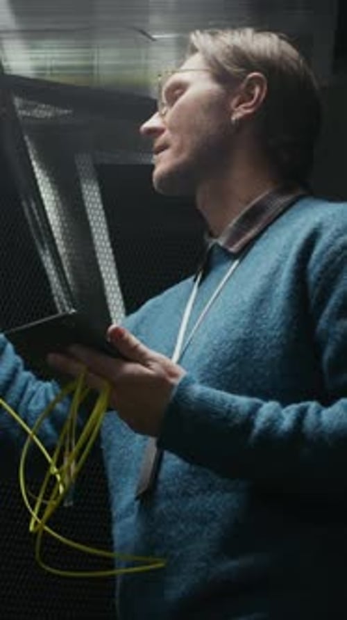 Vertical of Engineer Inspecting Server Rack with Tablet in Data Center