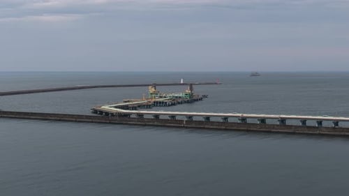 Ruhiges graues Meerwasser, das einen langen Betondamm und einen Industriepier unter bewölktem Himmel umgibt