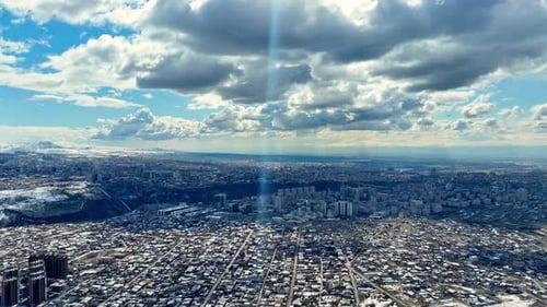 City sprawls beneath dramatic clouds, sunbeam pierces through