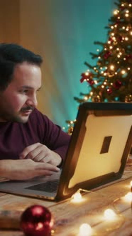 Young Man Chooses Christmas Gifts On The Computer In His Decorated House