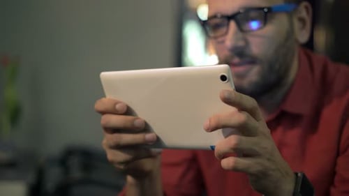 Young man browsing social media on his tablet computer at a cozy cafe at night