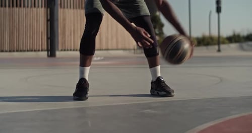 Person Dribbling Basketball on Court in Urban Park