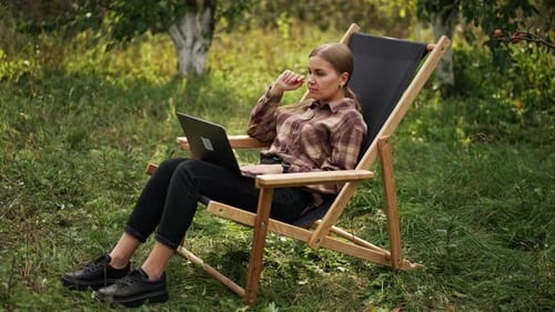 Freiberufliche junge Dame, die im Garten am Laptop arbeitet.