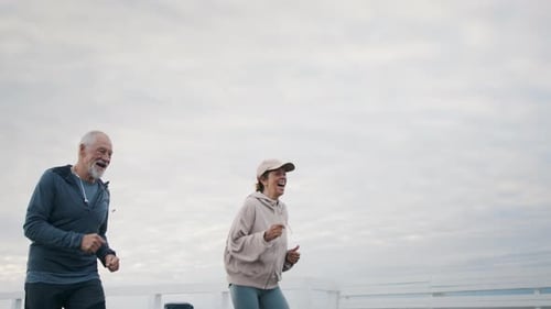 Senior couple runs together on seaside pier at dusk for vacation exercise
