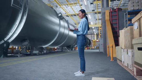 Woman Using Laptop Computer In Pipe Manufacturing Factory