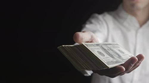 Hand Offers Hundred Dollar Bills on Black Background