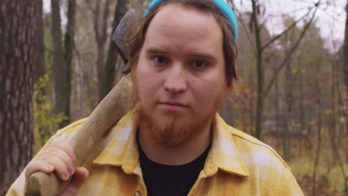 Ein bärtiger Holzfäller geht mit einer Axt auf der Schulter durch den Herbstwald