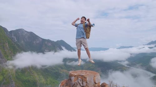 Asian Hiker Male Jumping Happy And Raising His Hand Celebrating Reaching Up Top Of Foggy Mountain