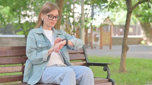 Young Woman Checking Wrist Watch on Park Bench