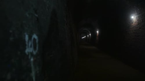 A dark tunnel with brick walls stretches into the distance, illuminated by evenly spaced lights alon