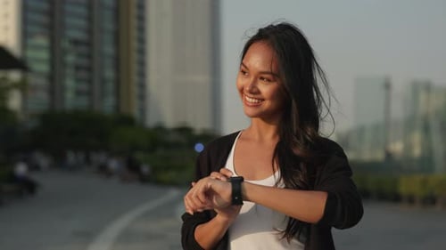 Portrait of Asian Woman Touches Smartwatch Screen and Stands in Urban Area