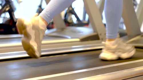 Female legs in sneakers run on a treadmill close-up, side view.
