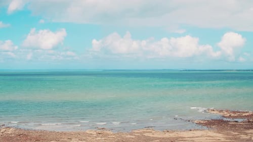Timelapse of fluffy white clouds billowing above a tropical blue, rocky beach that looks over the va